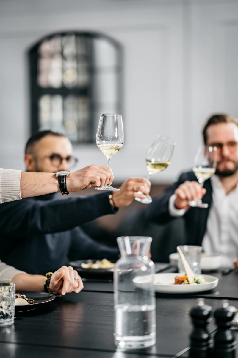 Freunde stoßen mit Weingläsern in elegantem Restaurant des Hotels an.