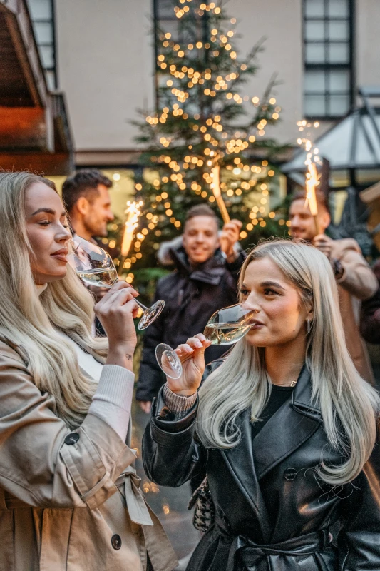Zwei Frauen stoßen mit Gläsern an, umgeben von weihnachtlicher Dekoration im Festgarten.