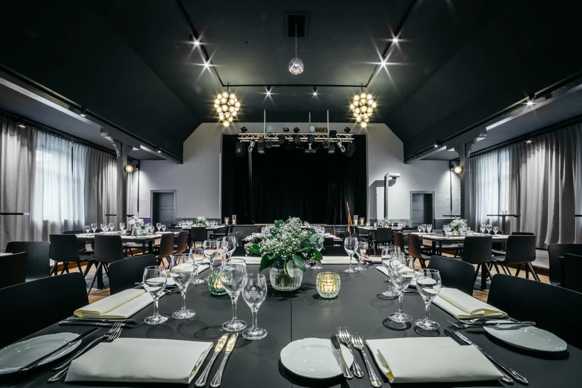 Eleganter Festsaal im Schwarzen Adler, festlich gedeckte Tische, Kronleuchter, Bühne.